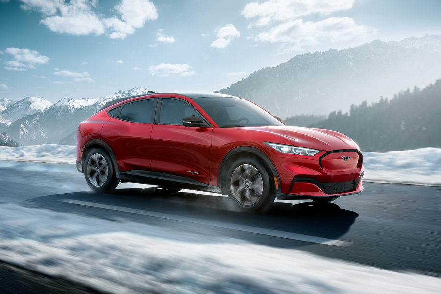 A red Ford Mustang Mach E drives along a snowy highway